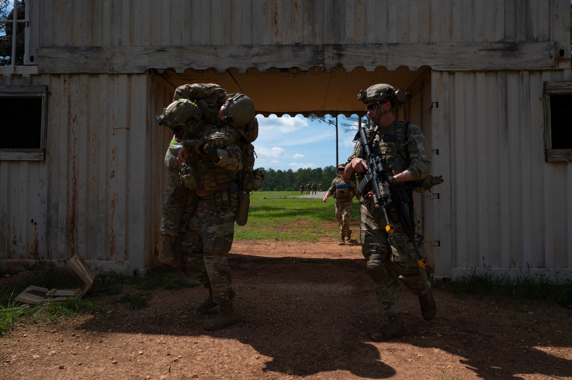 An Airman (left) fireman carries a simulated deceased body, with another Airman on his right watching over him.