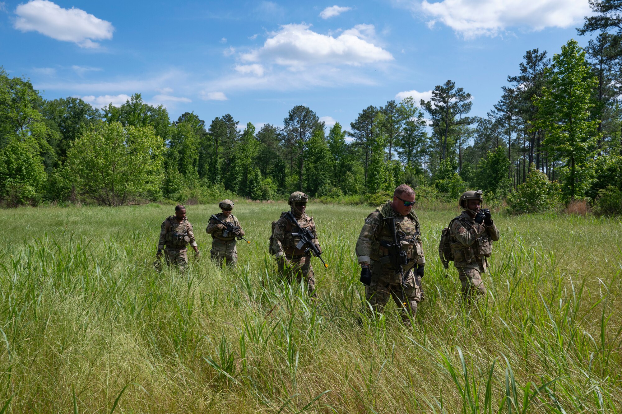 Five people walk through a grassy field.