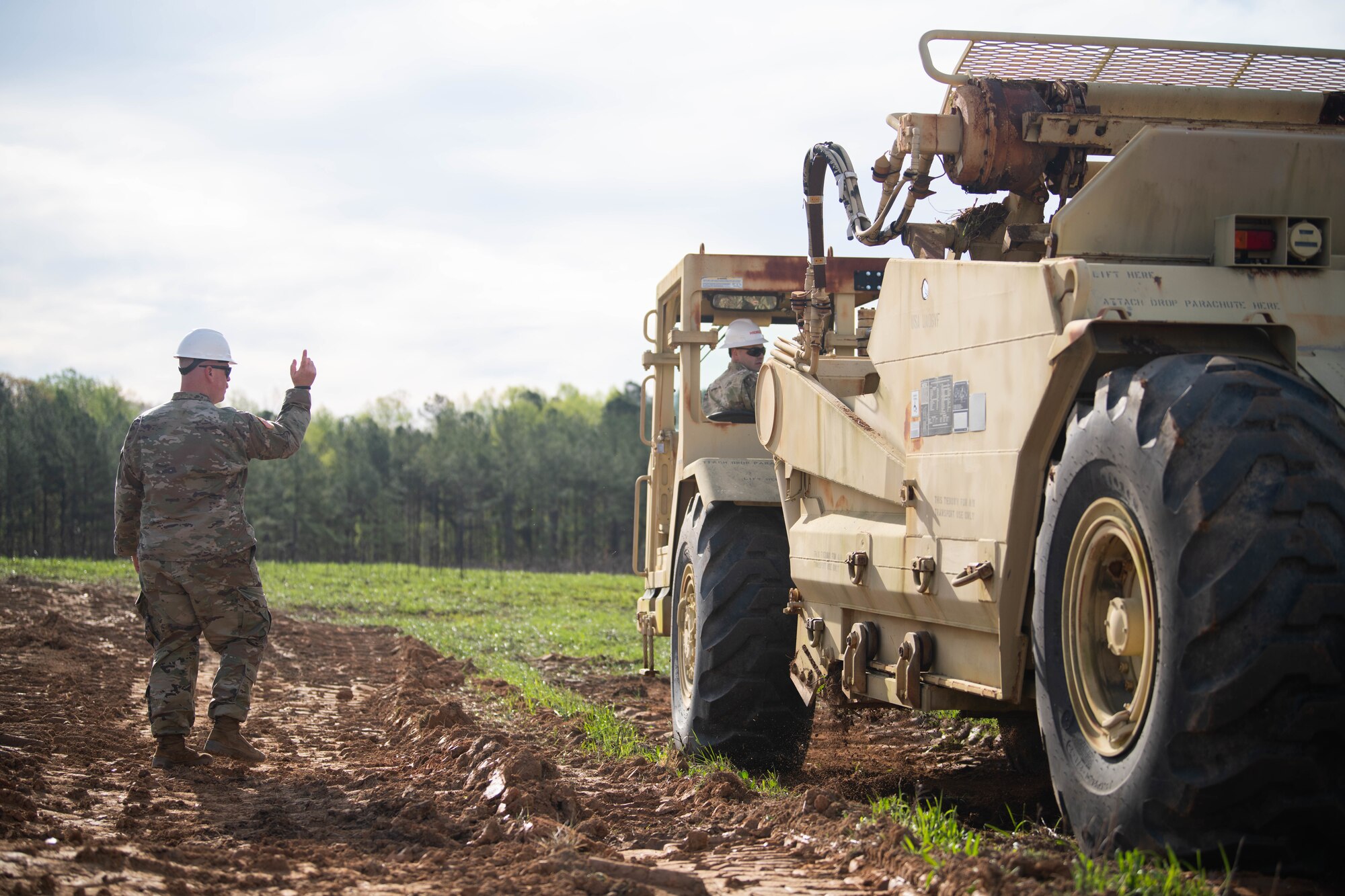 Airman directing another Airman driving heavy equipment.