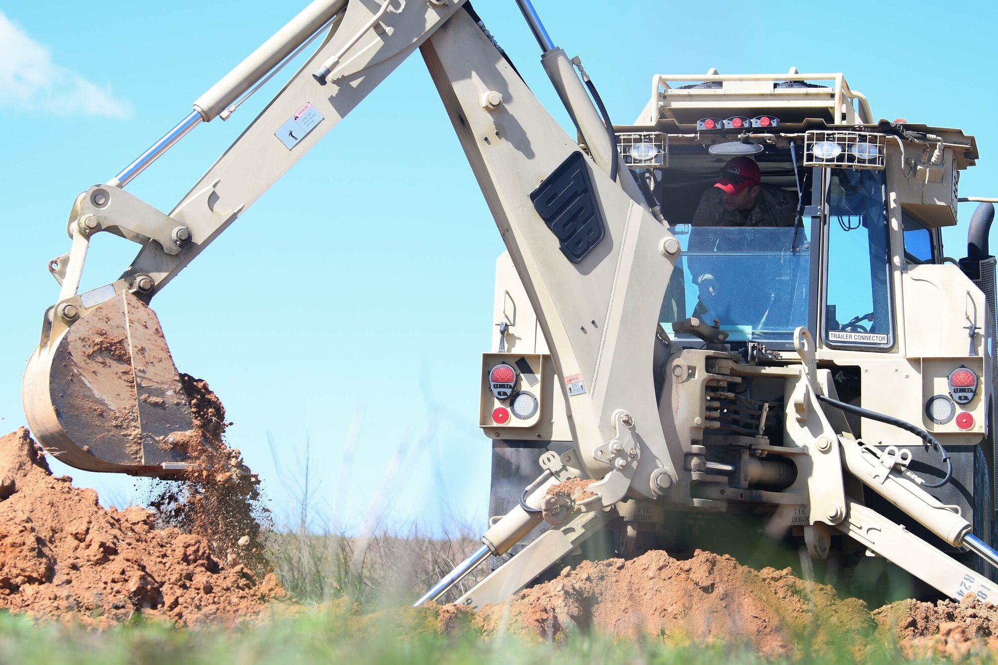 Airman operating a backhoe, scooping up dirt.