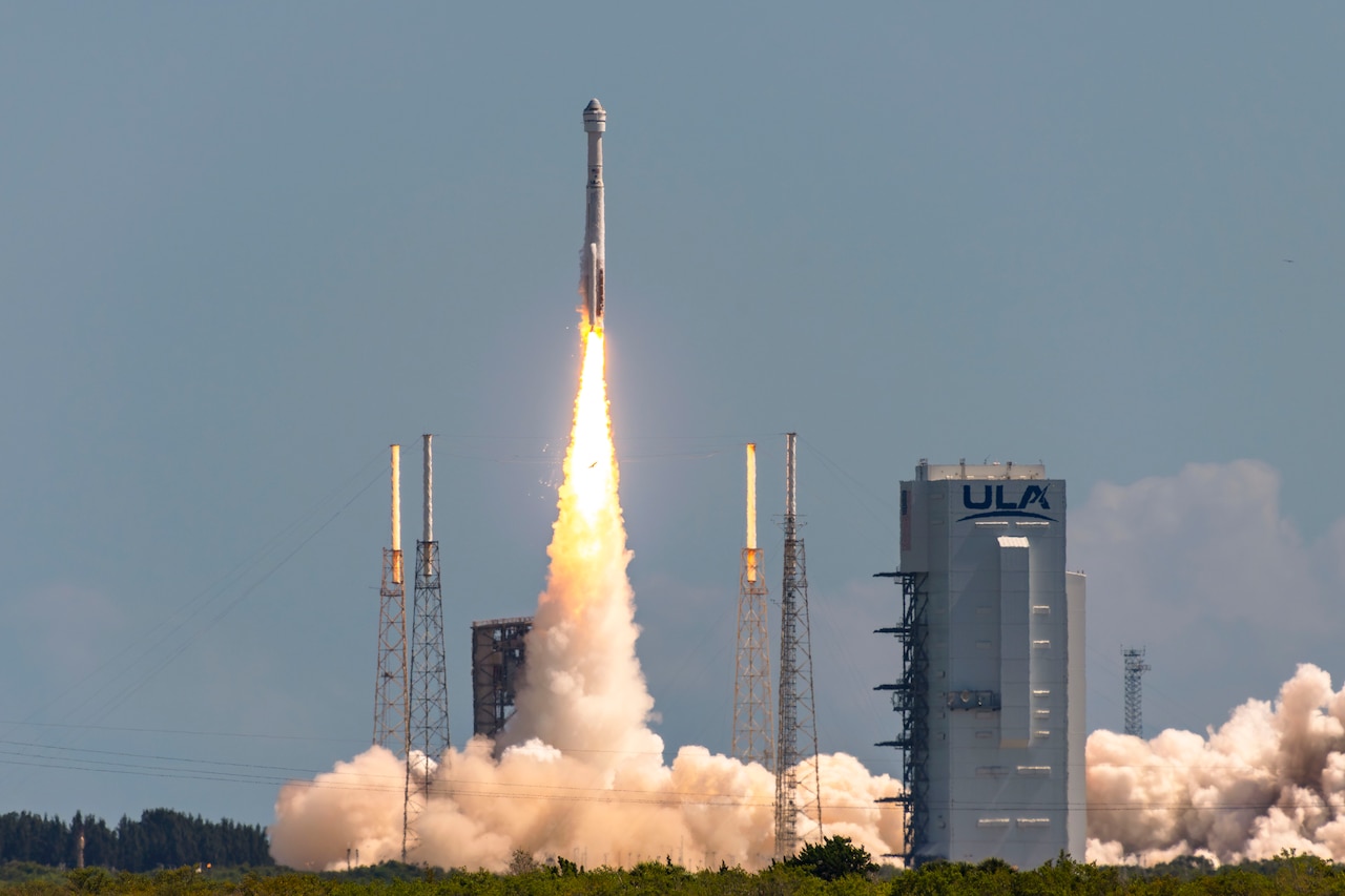 A rocket launches from a space station leaving behind plumes of smoke.