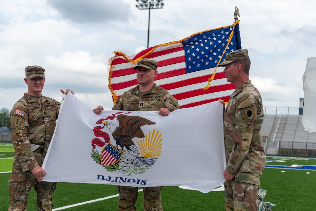 U.S. Army Capt. Matthew Rowe, center, the commander of Company A, 1st Battalion, 178th Infantry Regiment, Illinois Army National Guard, is presented a state of Illinois flag to take overseas during a mobilization ceremony in Peoria, Illinois, June 4, 2024.