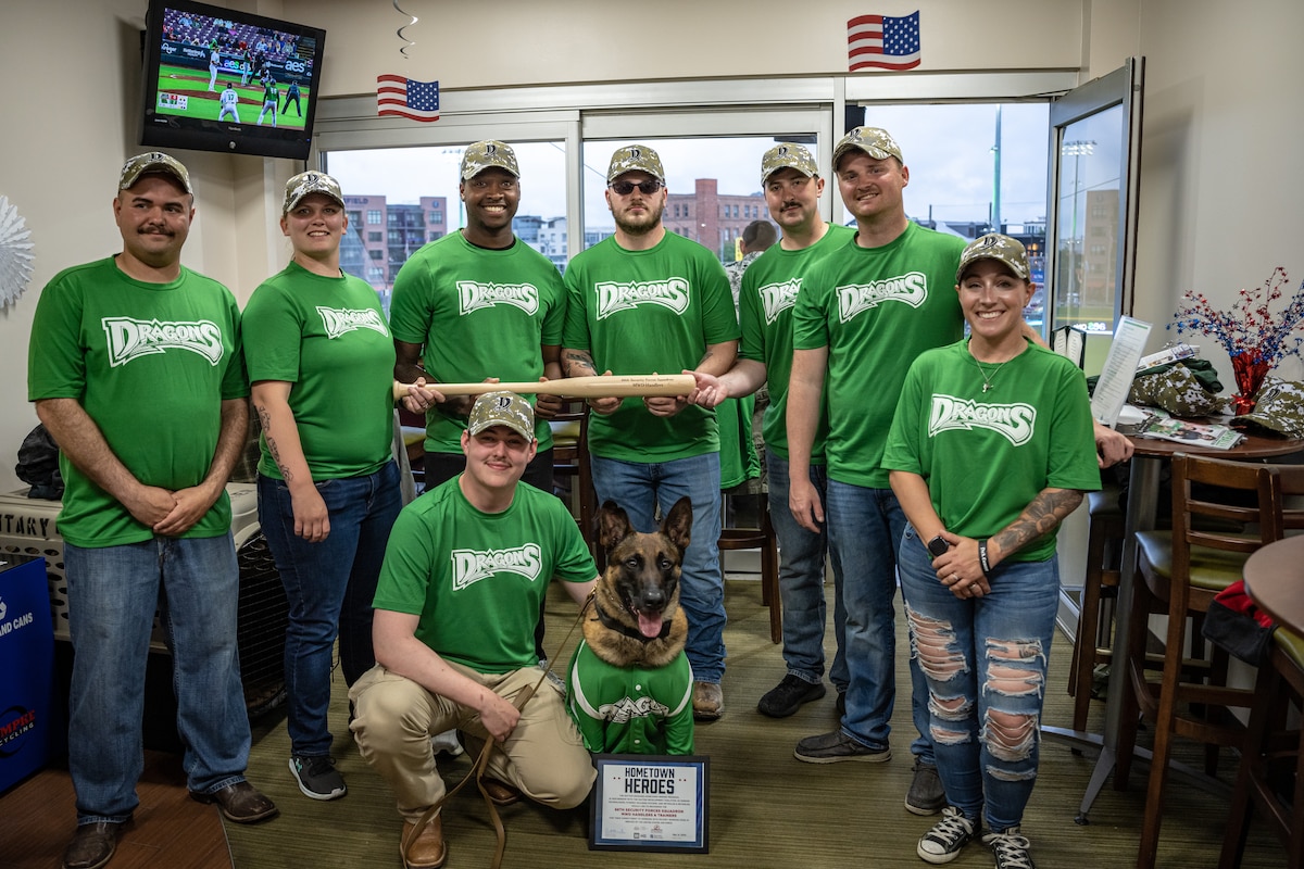 A group photo of eight people and one dog wearing green Dayton Dragons shirts holding an engraved baseball bat
