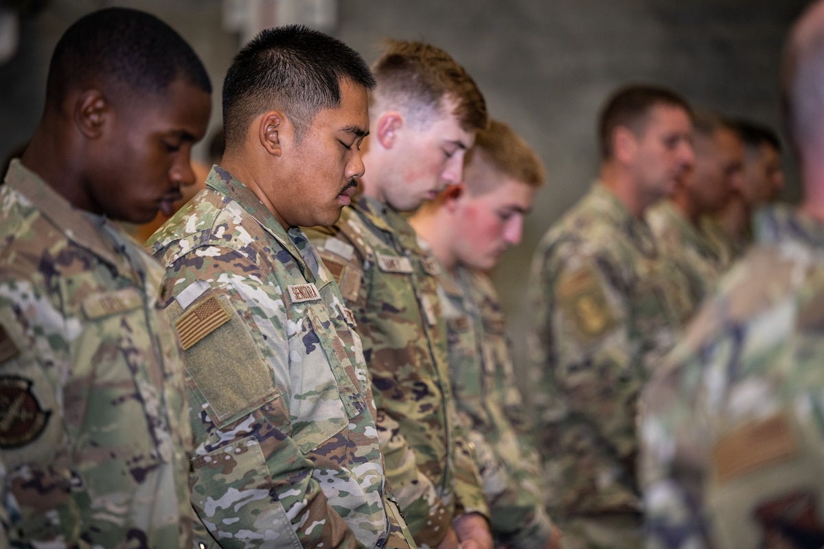 A group of service members stand with their heads bowed and eyes closed
