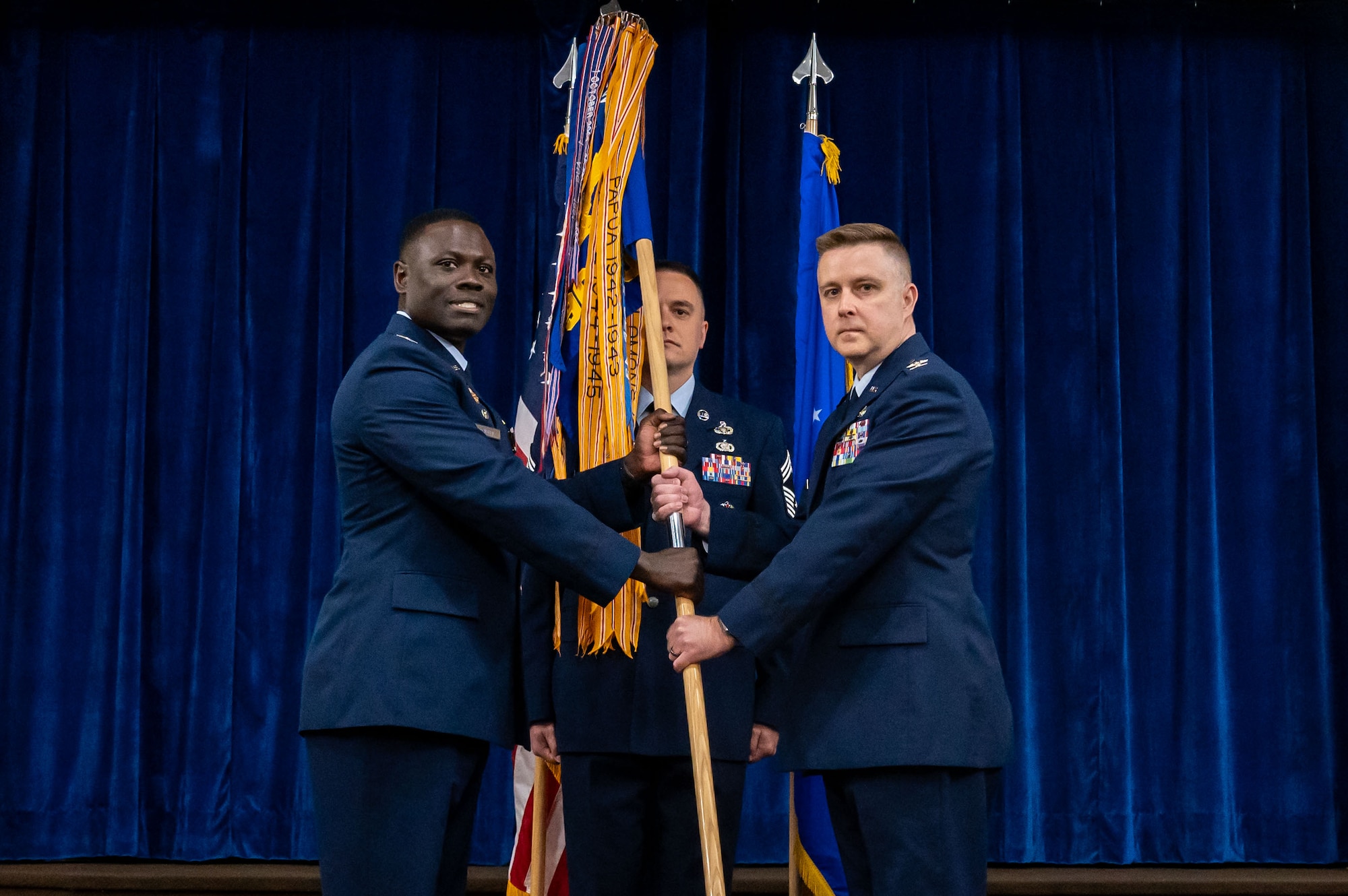 two uniformed individuals passing a flag between them