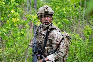 An Airman stands in a field with his kit and rifle.
