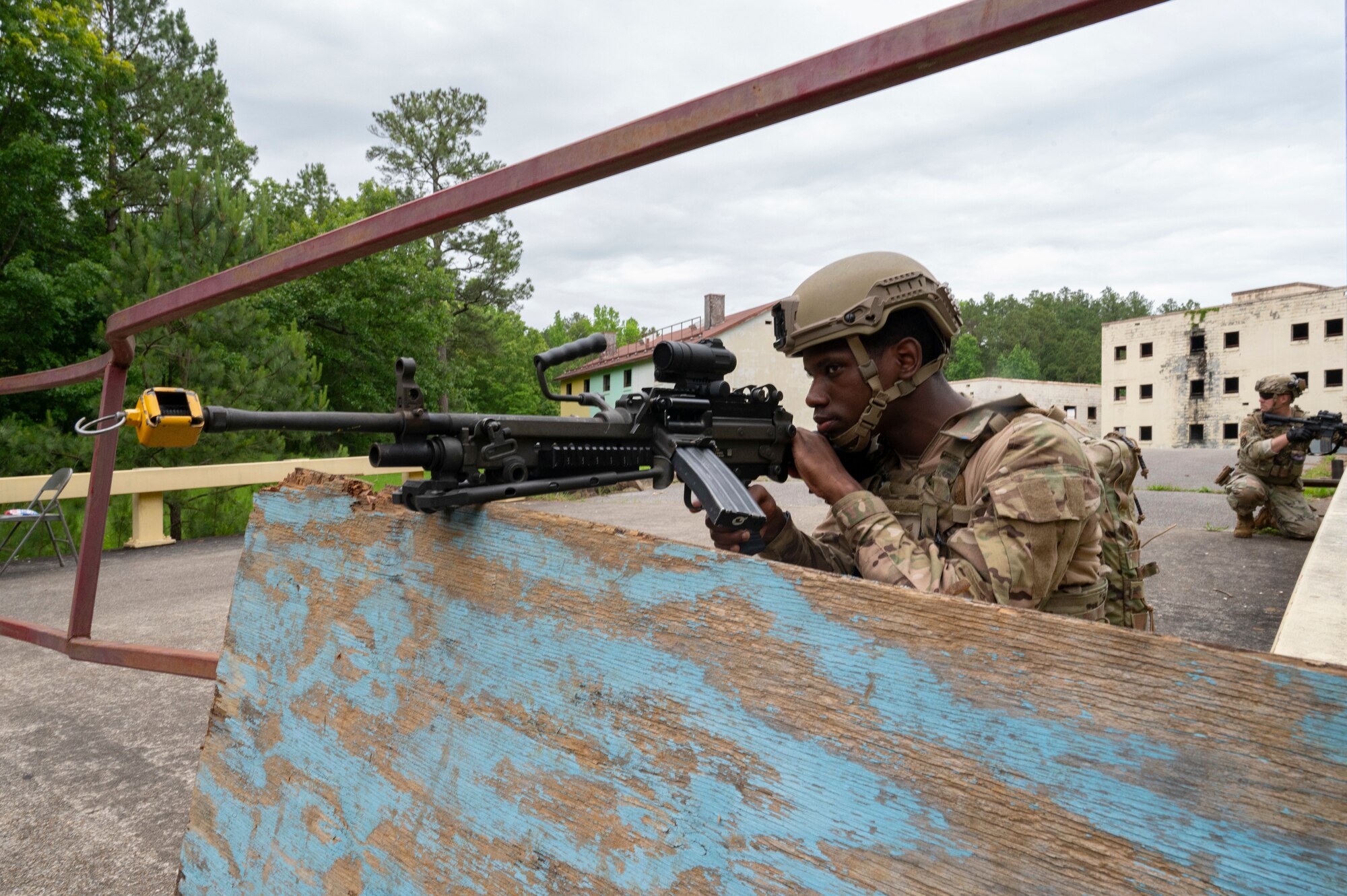 An Airman sits at a gate with a machine gun, pulling security.