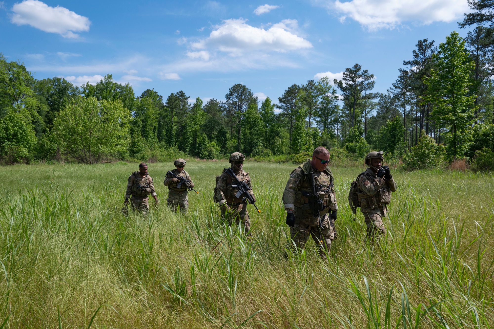 Five people walk through a grassy field.