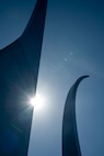 a photo of the U.S. Air Force Memorial shows large steel spires against the blue sky background with a partial view of the sun shining through