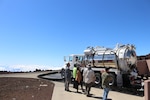 A fuel truck is parked on a barren lava field above the clouds.