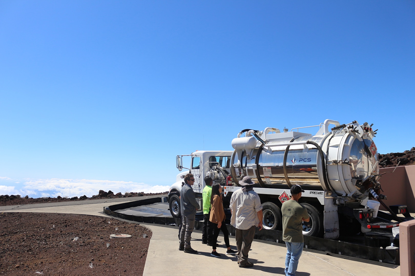 A fuel truck is parked on a barren lava field above the clouds.