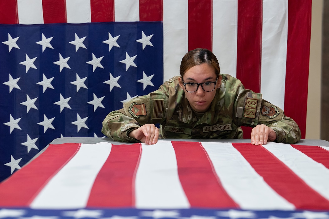 Senior Airmen Jocelyn Rosado, Air Force Mortuary Affairs Operations departures specialists, straightens the stripes on a U.S. flag