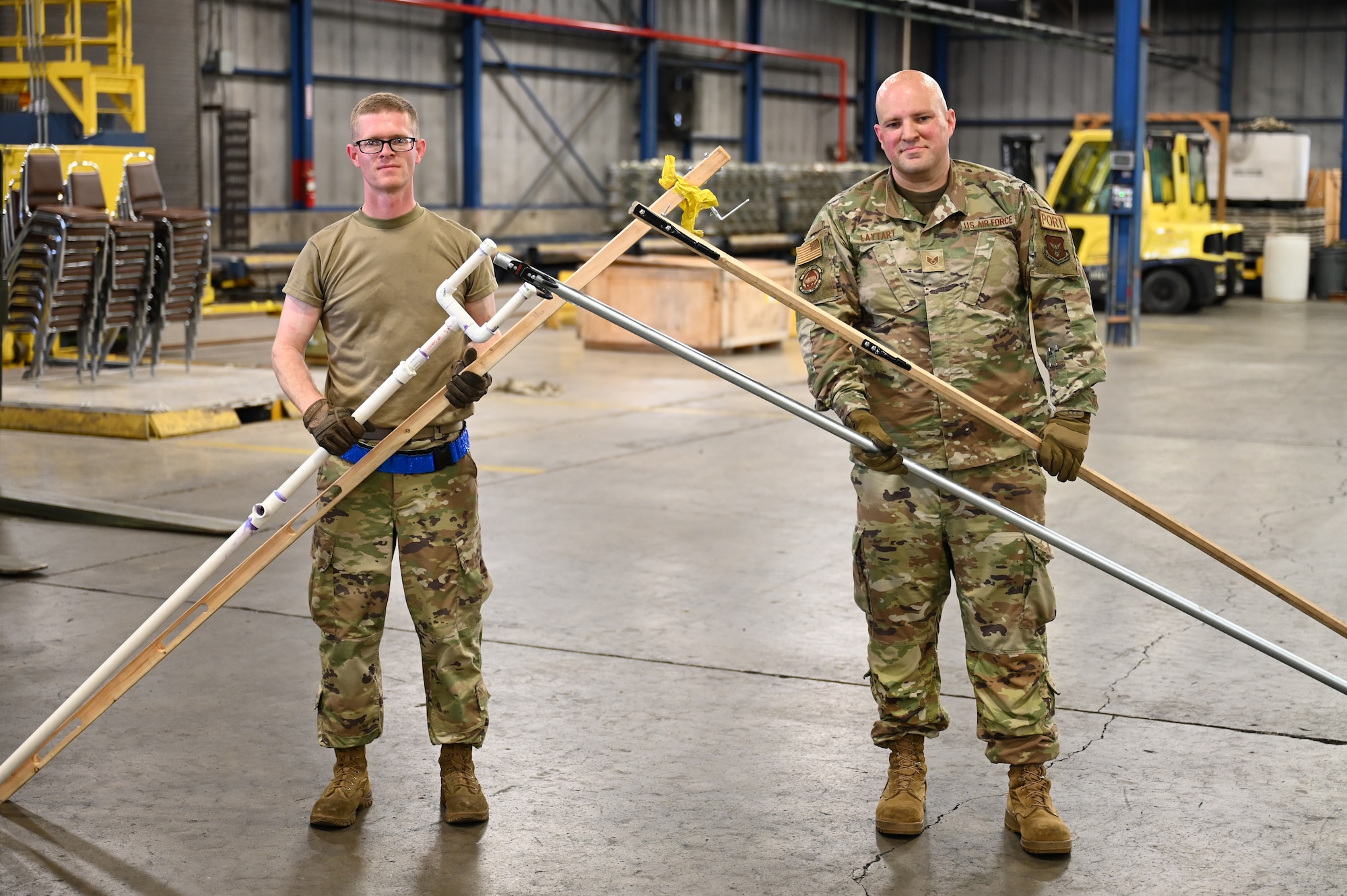 Staff Sgts. Daniel Schnaars and Kirk Laytart pose with the evolutions of their Pallet Spear tool net inside the cargo processing warehouse at Wright-Patterson Air Force Base, Ohio, May 4, 2024.