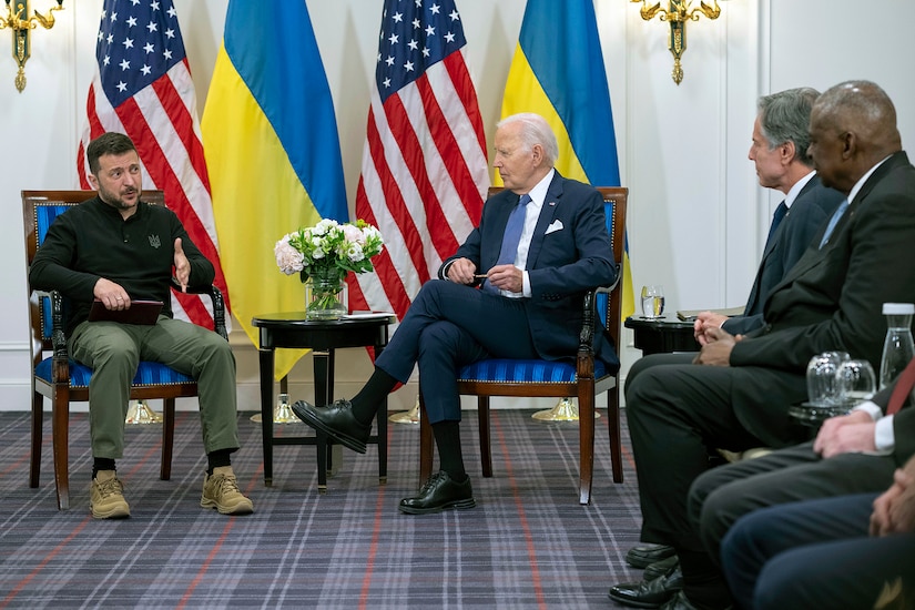 President Joe Biden sit by the Ukrainian President with flags behind them and three people in the audience.