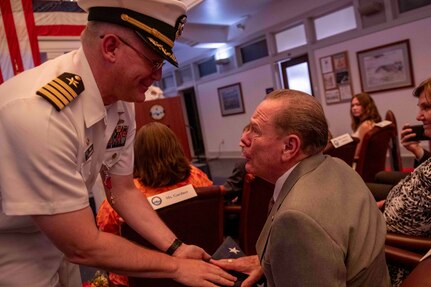 Capt. Sean Anderson, left, gives a flag to his father which was flown over the USS Carney (DDG 64) his first duty station, Tactical Training Group Atlantic (TTGL) his last duty station, Battleship Wisconsin (BB 64), and Lambeau Field at TTGL's change of command ceremony.