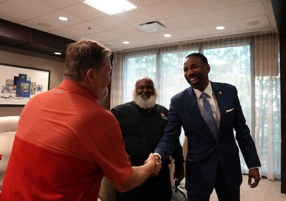 Atlanta Mayor Andre Dickens dressed in a navy blue suit shakes Brian Choate's hand who is dressed in a red polo shirt while Alou Rice dressed in a black shirt looks on.