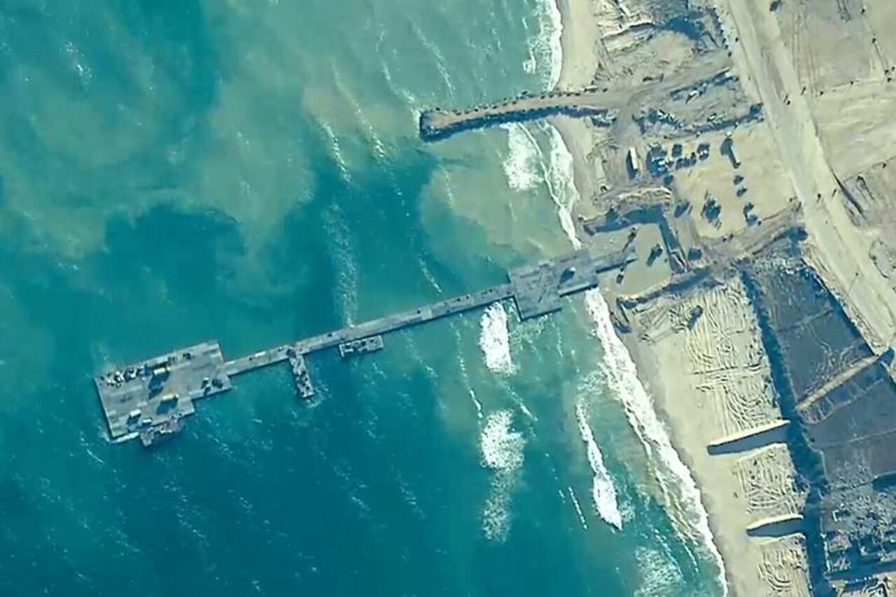 A view from space shows a long, slender, metal pier that extends from a sandy beach to roughly 800 feet out into the ocean.