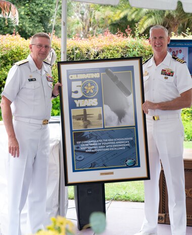 Vice Adm. Johnny Wolfe Jr., director of U.S. Navy Strategic Systems Programs (SSP) (left) presents a gift to Capt. Neil Sexton, Engineering Duty Officer (EDO) Schoolhouse commander (right), in honor of the school's fiftieth anniversary EDO School Thursday, June 6. SSP is the Navy command that provides cradle-to-grave lifecycle support for the sea-based leg of the nation's nuclear triad and for approximately 70 percent of the U.S.'s deployed strategic nuclear assets. EDOs supporting SSP are responsible to ensure the strategic weapon system is deployable and ready to support the vital strategic deterrence mission of America's Warfighting Navy. The EDO school-established in 1974 and founded by Naval Sea Systems Command Commander Vice Adm. Robert C. Gooding-provides education to improve the professional proficiency of EDOs through training in plans, programs, policies, and procedures that drive the life-cycle engineering of naval ships and systems. (U.S. Navy Photo by Lt. Jennifer Bowman/Released)