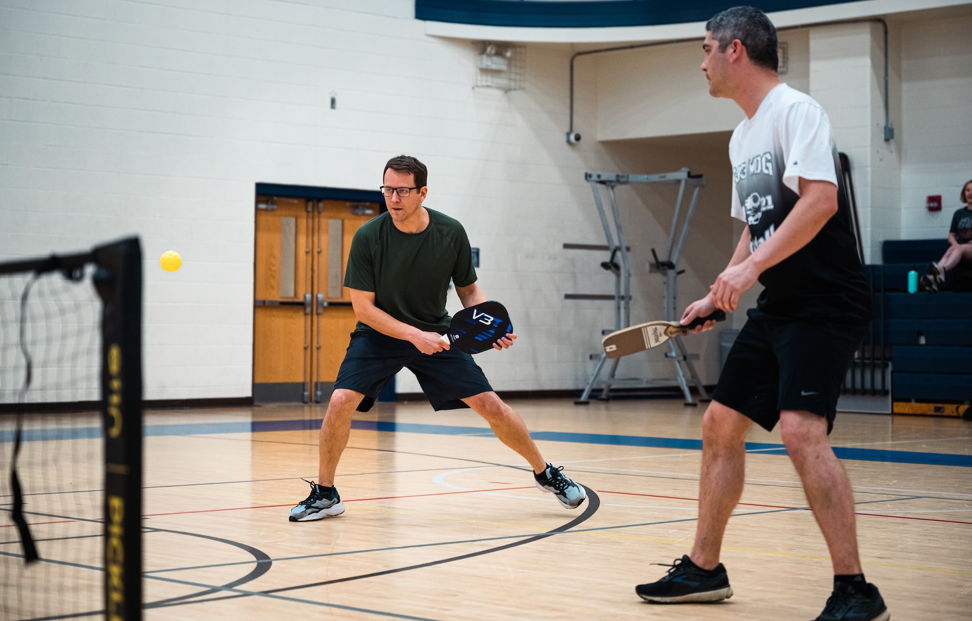 A man prepares to hit a yellow pickleball in a gym