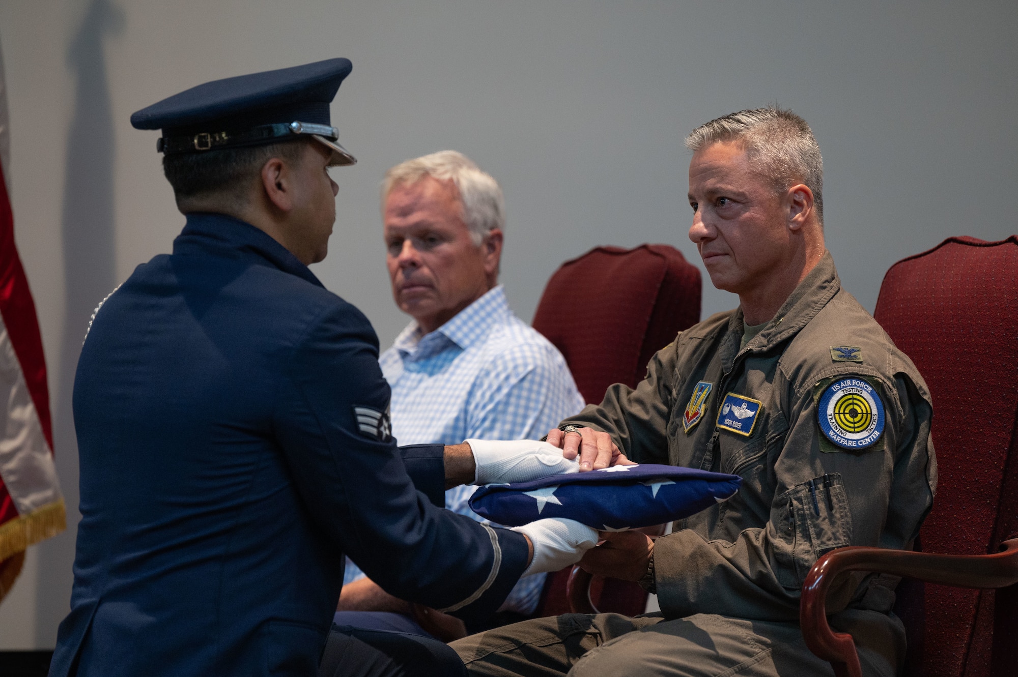 An honor guardsman hands an American flag to a man siting in a chair.