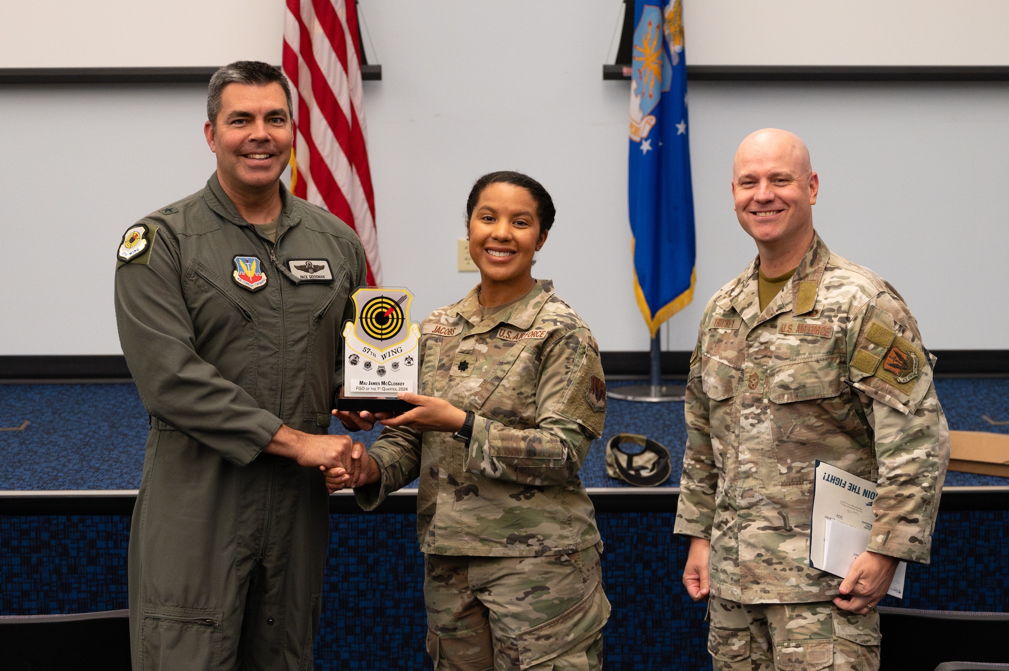 Two men shake hands and hold an award while a third man stands on the side.