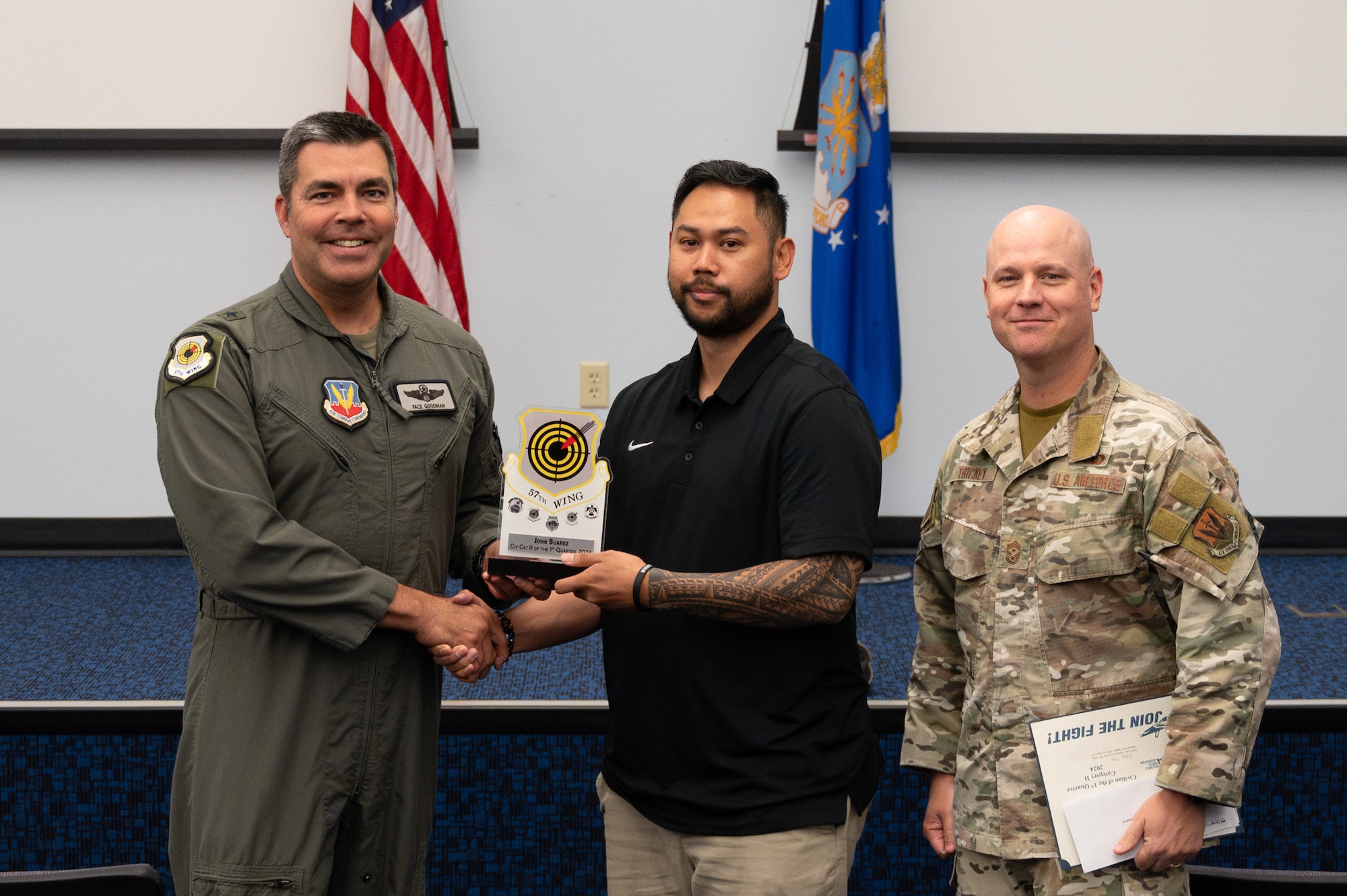 Two men shake hands and hold an award while a third man stands on the side.