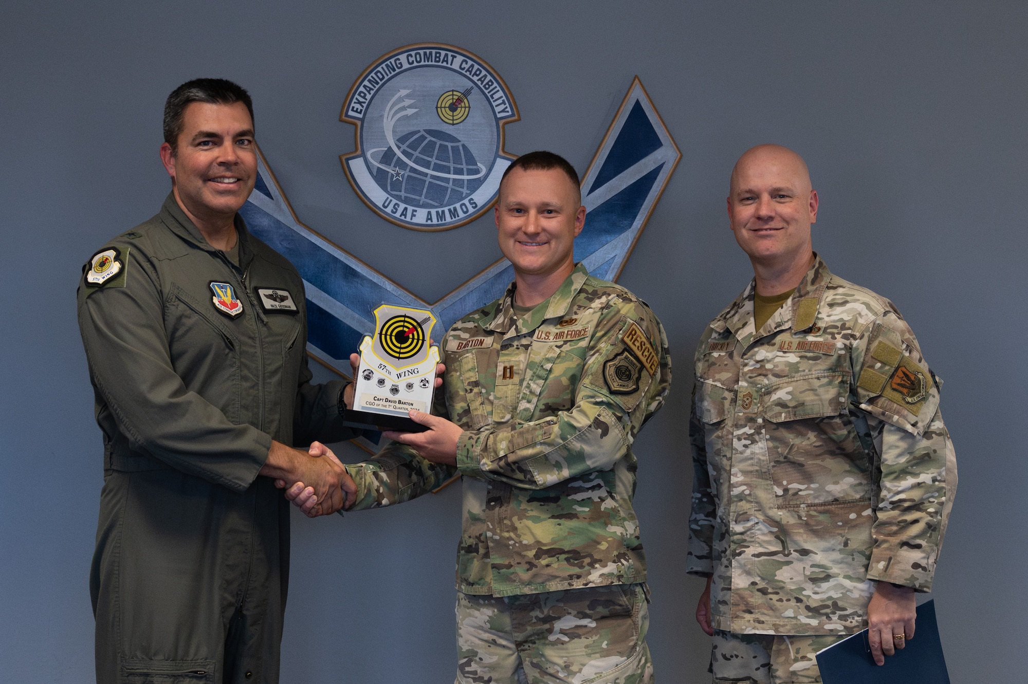 Two men shake hands and hold an award while a third man stands on the side.