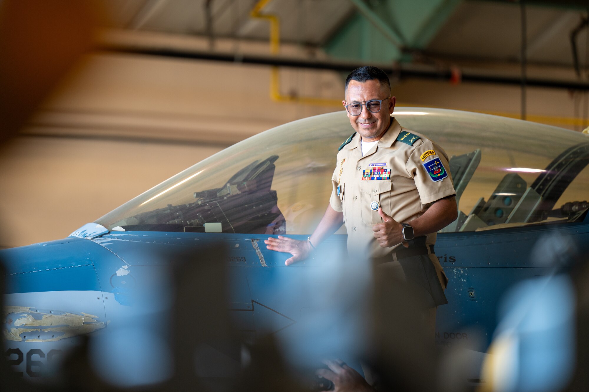 A man poses for a photo with a thumbs up next to an F-16 Fighting Falcon.