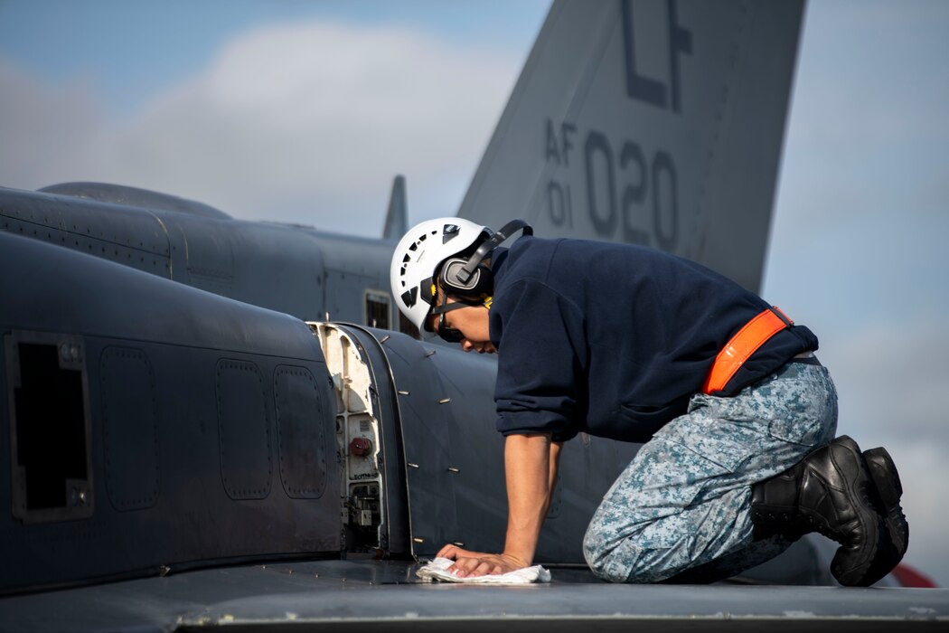 A maintainer crouches on the wing of an F-16 wing while conducting maintenance on the aircraft.