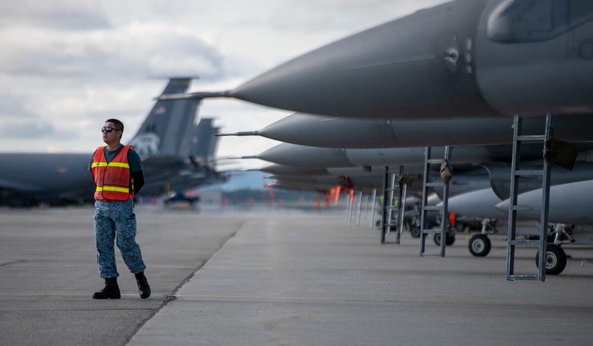 A male maintainer walks in front of F-16s on the flightline.