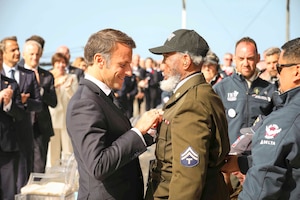The French president puts a pin on a veteran’s uniform as others applaud in the background.