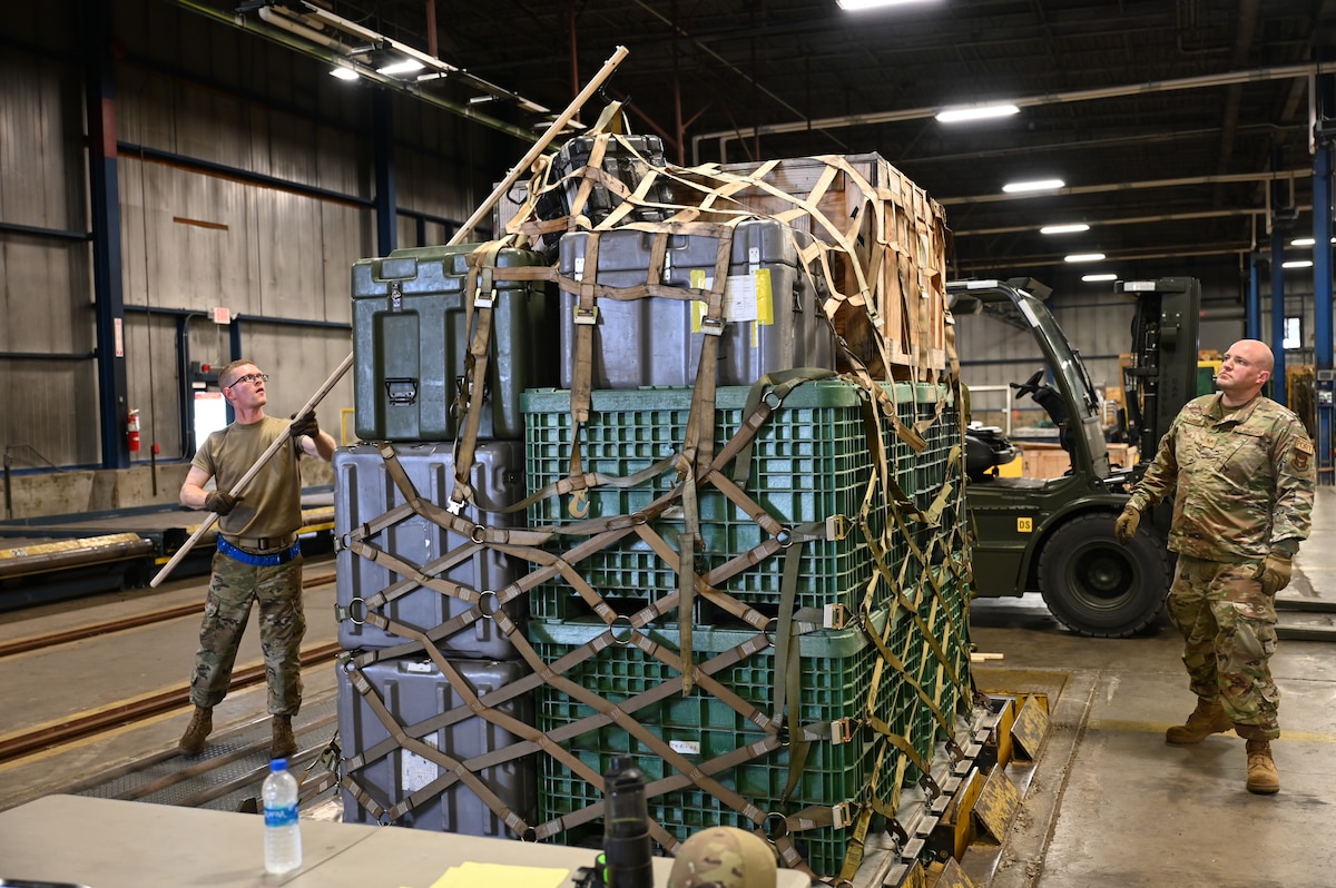 Staff Sgt. Daniel Schnaars, 87th Aerial Port Squadron air freight representative, uses a pallet spear to grab and lift a top net from a tall pallet so Staff Sgt. Kirk Laytart, 87th APS passenger service representative, can pull it off and away from the pallet during the breaking down process at Wright-Patterson Air Force Base, Ohio, May 4, 2024. The Airmen are developing the spear to replace the inefficient ladder system currently in use to remove nets from pallets and would also be a more safe option.