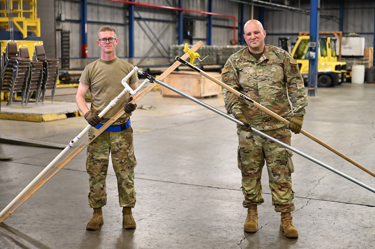 Staff Sgts. Daniel Schnaars and Kirk Laytart pose with the evolutions of their Pallet Spear tool net inside the cargo processing warehouse at Wright-Patterson Air Force Base, Ohio, May 4, 2024.