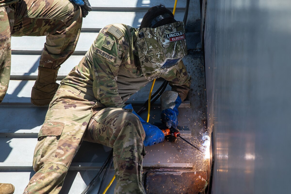 A soldier in uniform operates a welder aboard a military vessel.