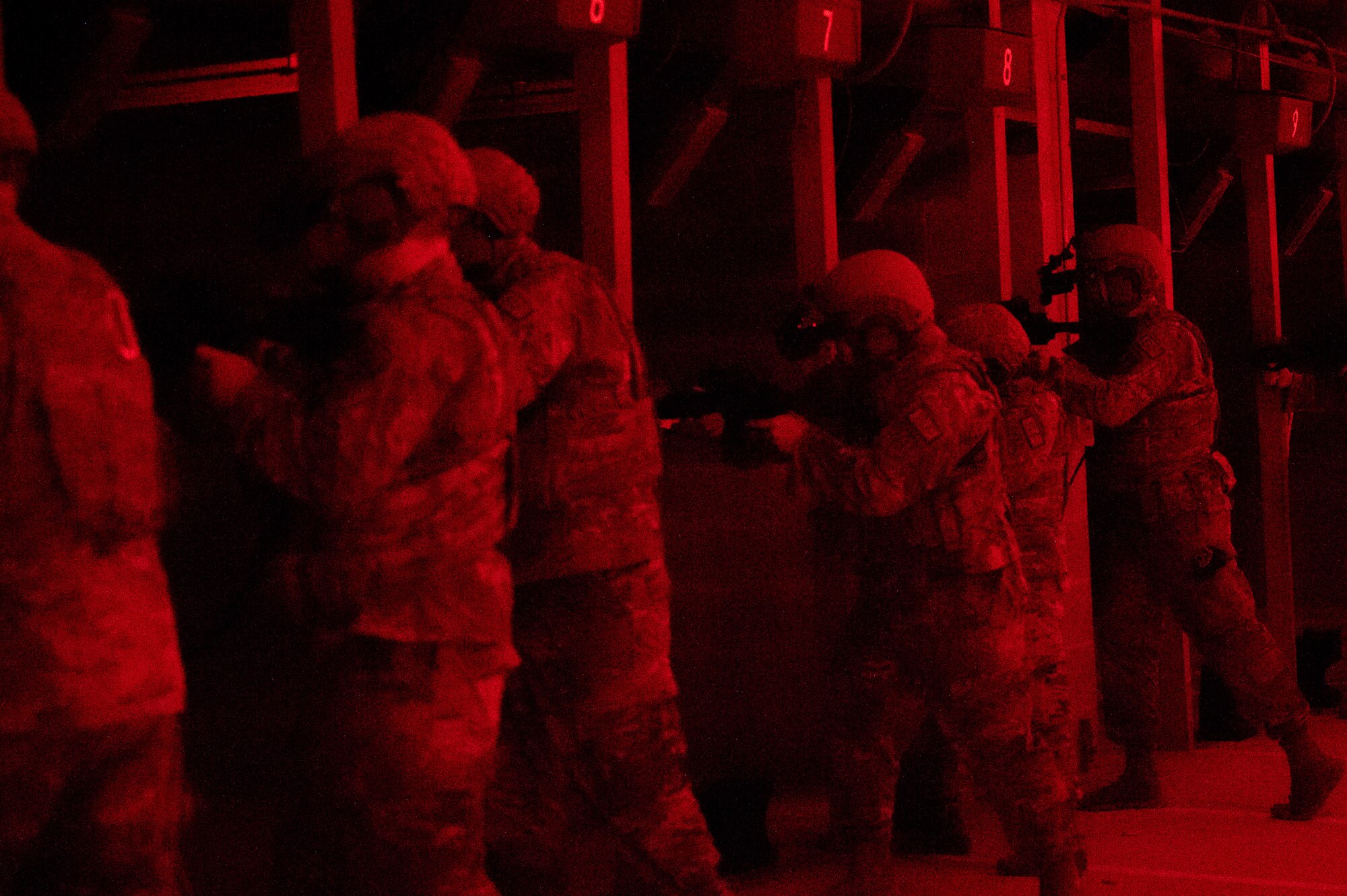 U.S. military members' backs, leaning over a barricade at a range. All appear to be holding weapons.