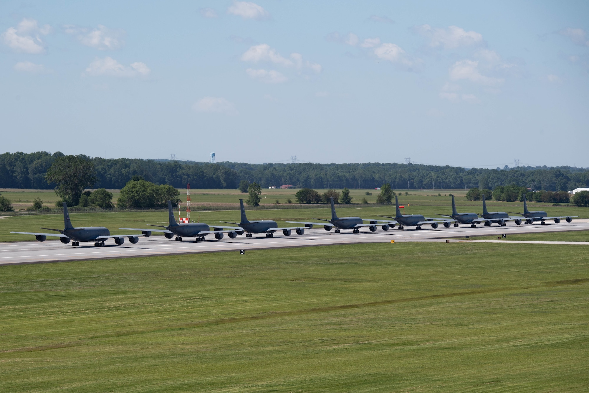 Multiple KC-135R Stratotankers taxi on a runway, out of the frame, moving from left to right. The photograph appears to be taken from a height significantly above the aircraft and runway.