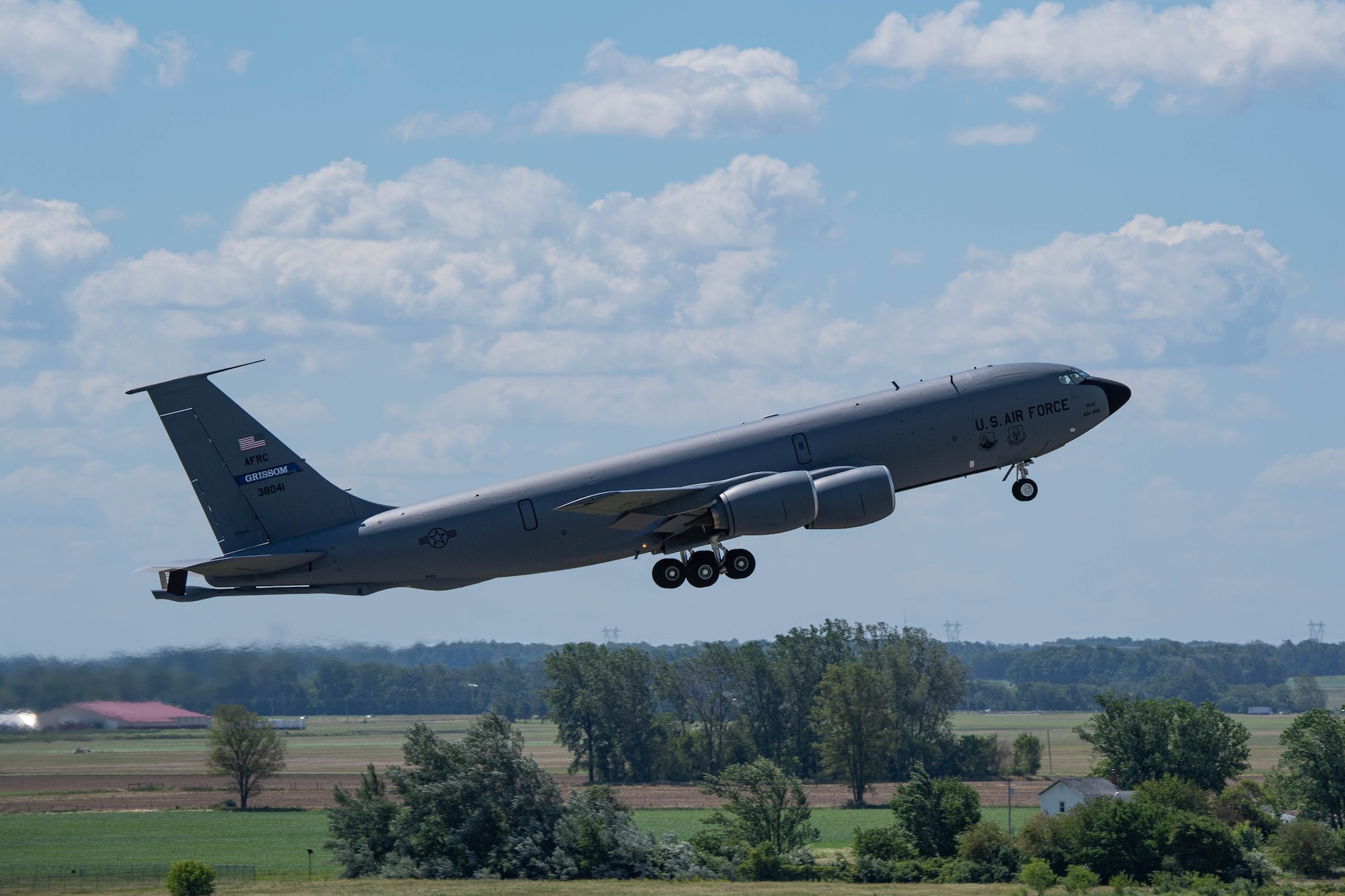 A KC-135R Stratotanker takes off, moving left to right in the photograph. In the background, land and sky.