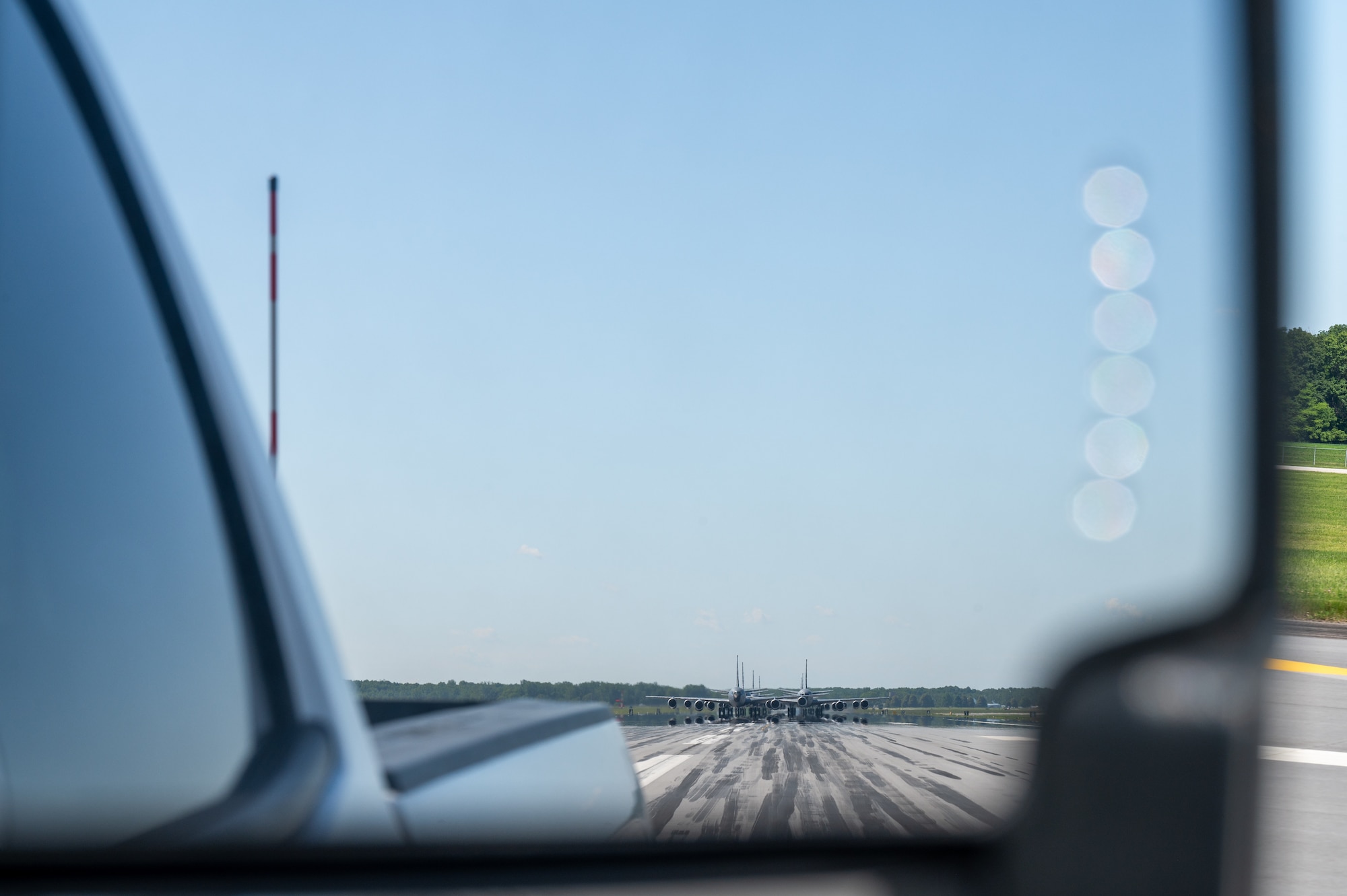 The rearview mirror of a truck. In the mirror, off in the distance, multiple KC-135R Stratotanker aircraft.