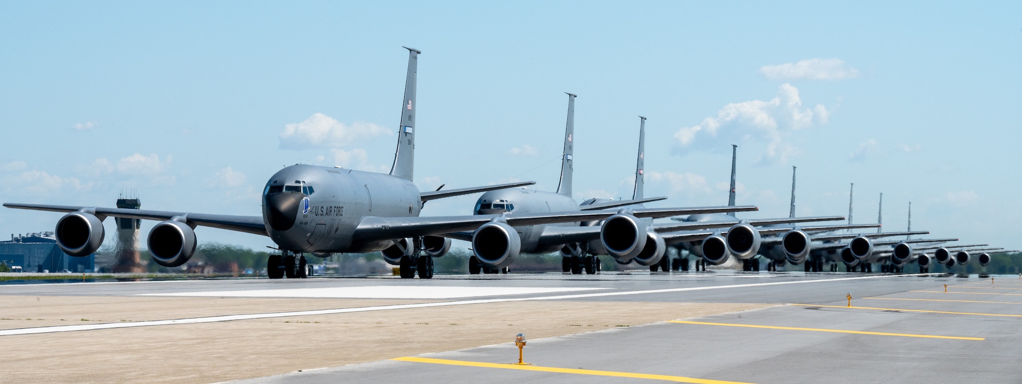 A partial side view of a KC-135R Stratotanker formation. In the background, an air traffic control tower.