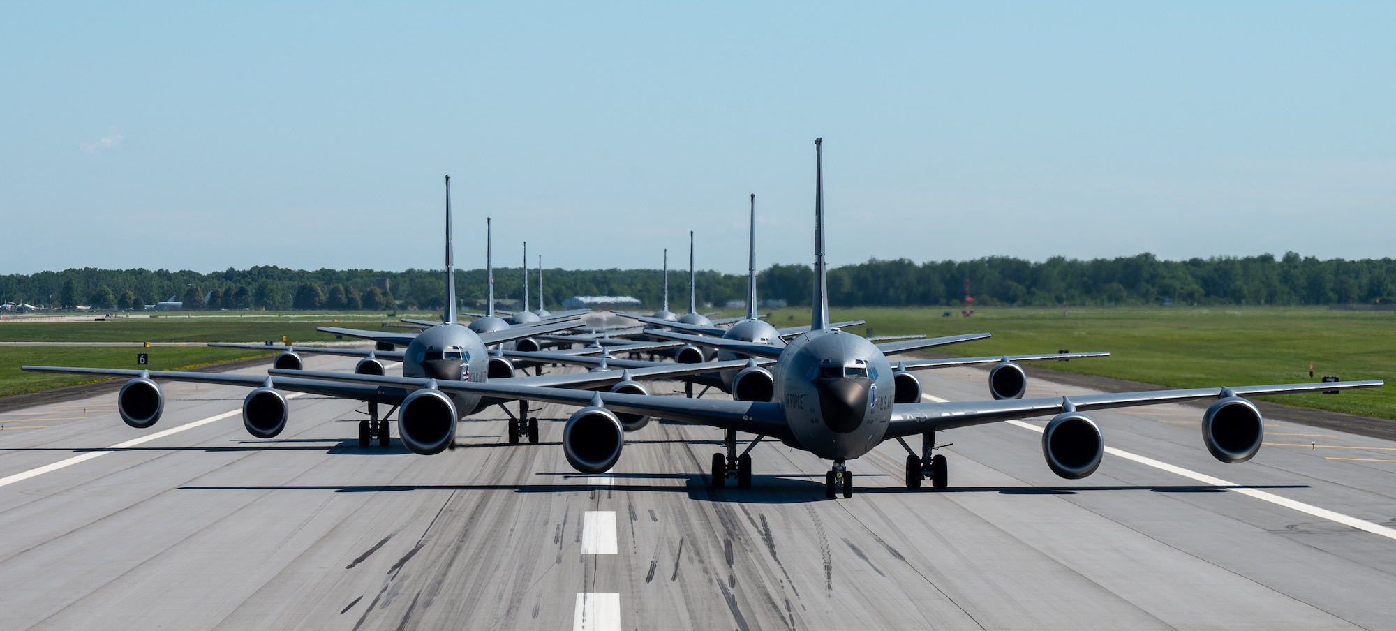 Eight KC-135R Stratotankers are lined up on a runway in a staggered formation. The photograph shows the head-on view of the formation.