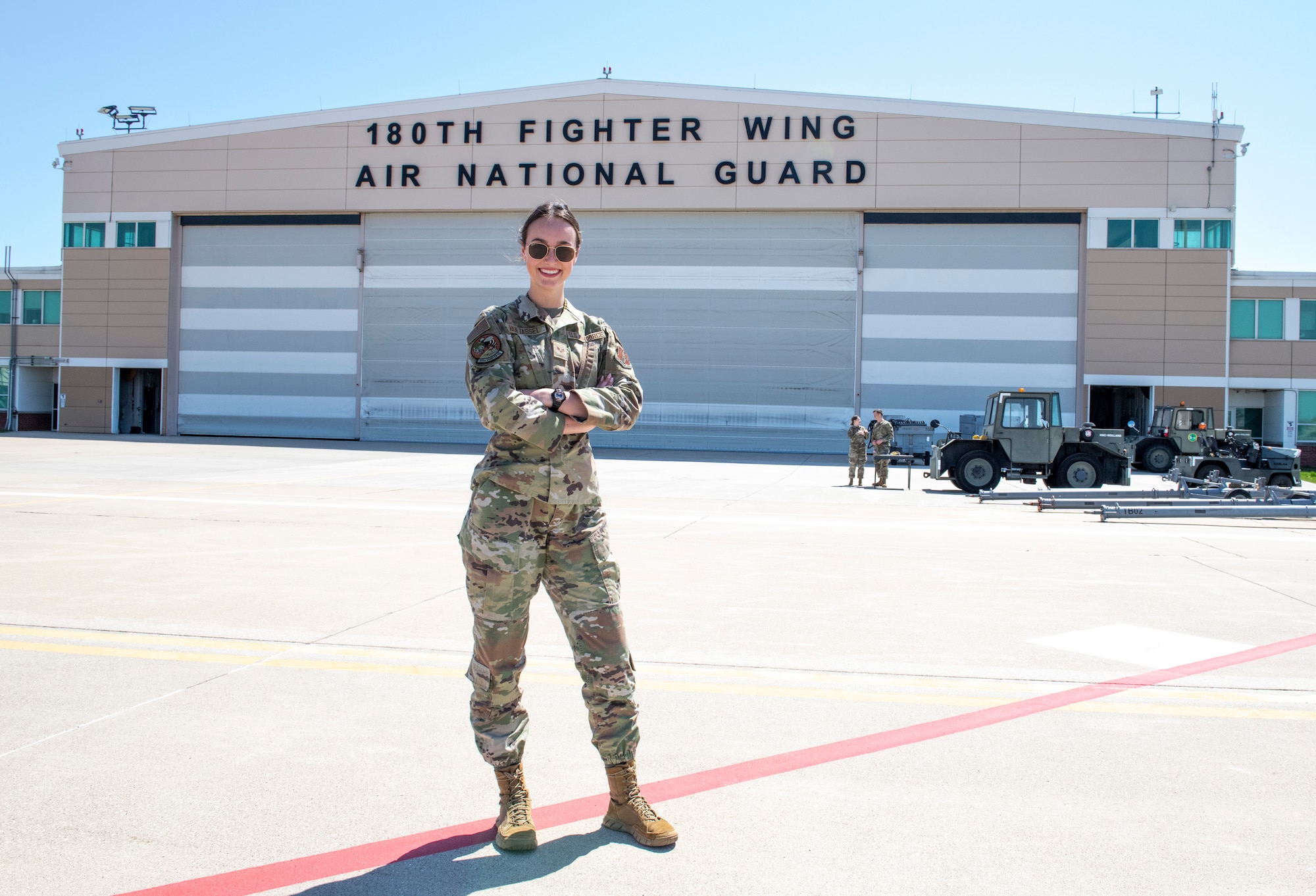 Woman poses in front on airplane hangar.
