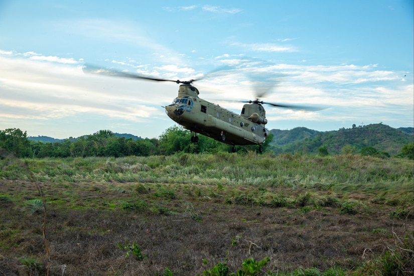 A military aircraft lands in a grassy field during daylight.