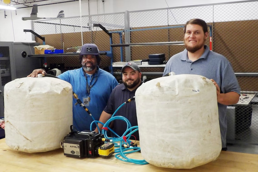 Three engineers stand with an inflated heavy lift kit.
