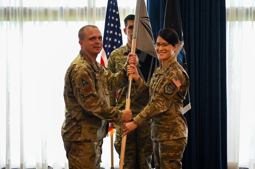 Two service members hold a flag as another stands in the background.