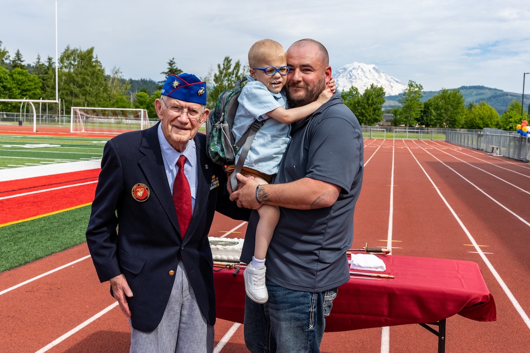 Arlan Russell, center, the youngest Marine present, and Harold Richard Throm, left, the oldest Marine present, pose for a photograph after a cake cutting during an Honorary Marine ceremony at Orting Middle School in Orting, Wash., June 8, 2024. The title of Honorary Marine is an honor bestowed by the Commandant of the Marine Corps to civilians who have made extraordinary contributions to the Marine Corps. The program began in 1992 and is intended to strengthen the bond between the American people and the Marine Corps. Notable Honorary Marines include Chuck Norris, Gary Sinise, and Joe Rosenthal. Russell is the 109th person to earn the title of Honorary Marine. (U.S. Marine Corps photo by Staff Sgt. Courtney G. White)