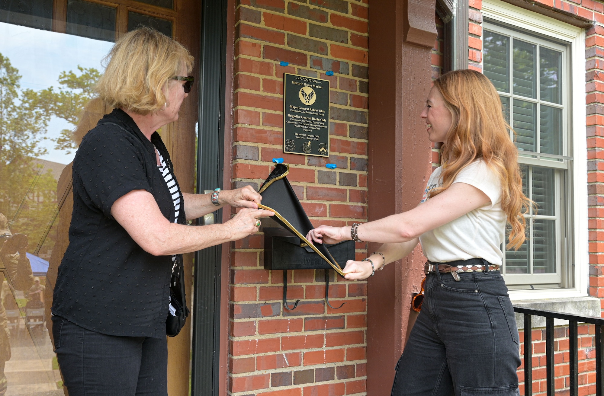 Two women pull a sheet off a sign.