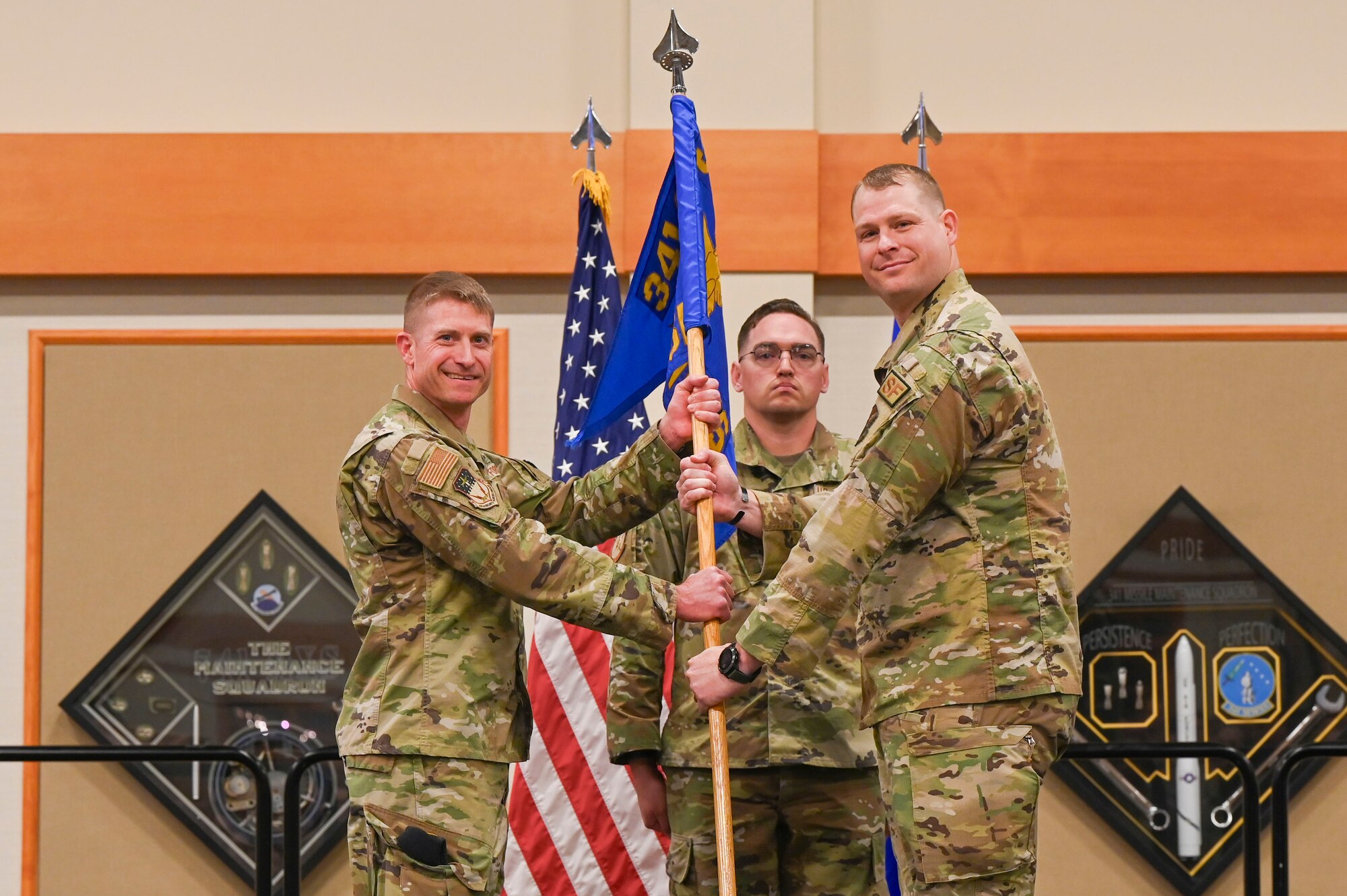 Two people holding onto the pole of a flag and lookin at the camera.