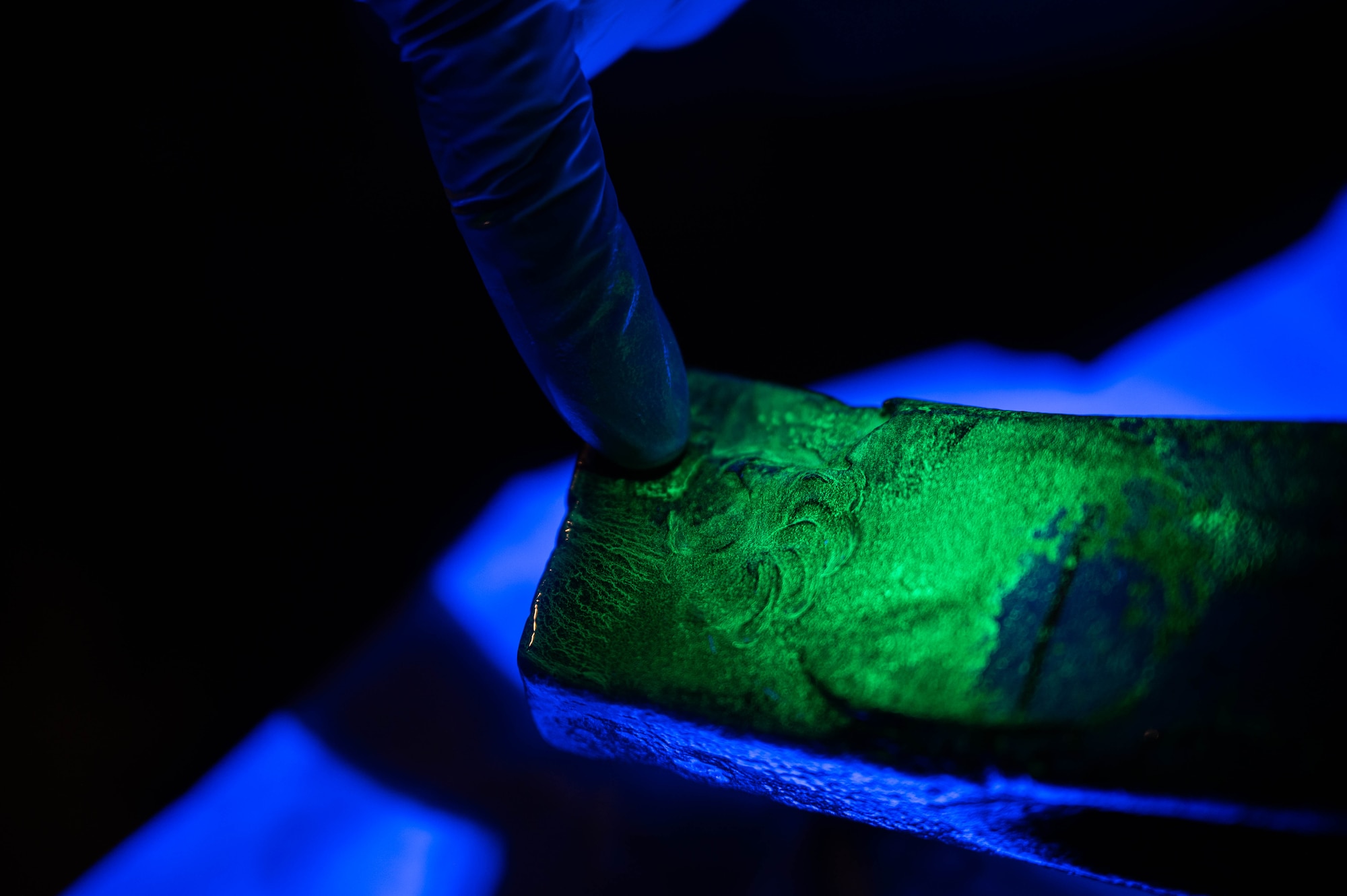 U.S. Air Force Senior Airman Jonathan Macias, 5th Maintenance Squadron non-destructive inspection (NDI) journeyman, points out damage from a MHU-97/E part during a magnetic particle inspection at Minot Air Force Base, North Dakota, June 6, 2024. The black light allows NDI Airmen to locate cracks and imperfections on B-52H Stratofortress parts and aircraft support equipment. (U.S. Air Force photo by Airman 1st Class Luis Gomez)