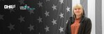 Woman wearing jacket smiles and stands in front of American flag.