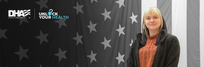 Woman wearing jacket smiles and stands in front of American flag.
